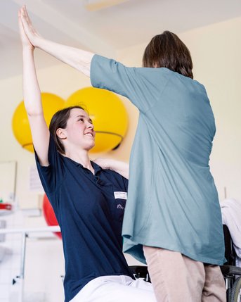 Eine Physiotherapeutin des SRH Fachkrankenhaus Neresheim unterstützt eine Patientin beim Arm heben.